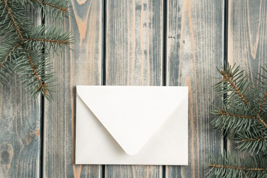White envelope on on gray wooden background with branches of Christmas tree. New year envelope. Top view. Copy space. Greeting and congratulations on Christmas eve