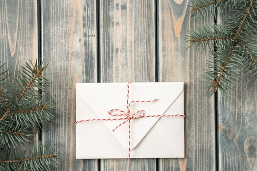 White envelope on on gray wooden background with branches of Christmas tree. New year envelope tied with cord with bow. Top view