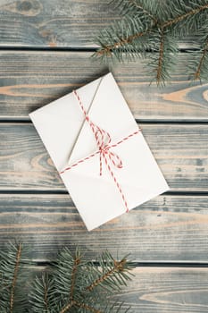 White envelope on on gray wooden background with branches of Christmas tree. New year envelope tied with cord with bow. Top view. Vertical