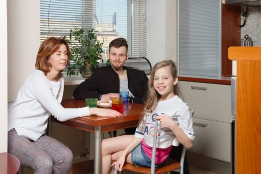 family on the kitchen behind the table drinking beverage and eating sweets