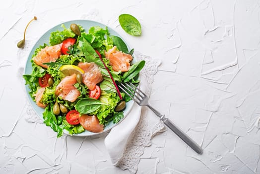 Fresh green salad with smoked salmon, cherry tomatoes and capers on white table background close up