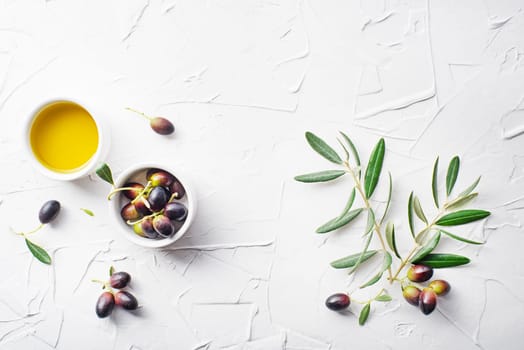 Olive oil in bowl with fresh olives fruit and olive branch on white background close up