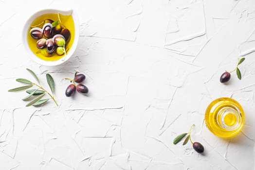 Olive oil in bowl with fresh olives fruit and olive branch on white background close up