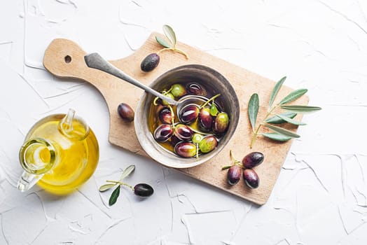 Olive oil in bowl with fresh olives fruit and olive branch on white background close up