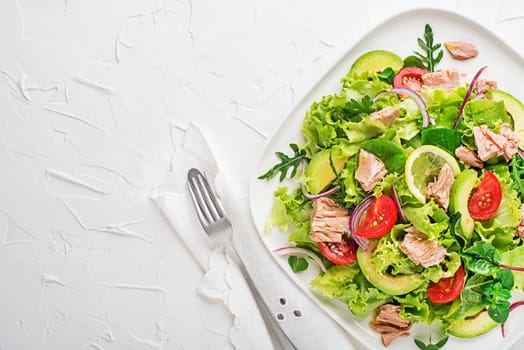 Fresh green leafy salad with tuna avocado and tomato on white table background. Concept for a tasty and healthy meal