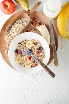 A bowl of dry granola and muesli served with fresh fruit and nuts. Oatmeal plate. Healthy food, diet. Top view.