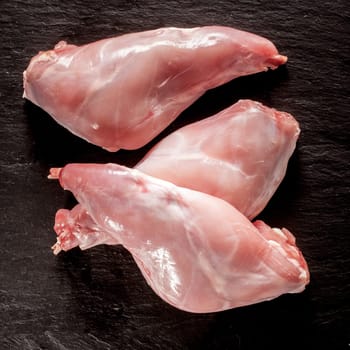 Uncooked fresh wild rabbit or hare haunches ready for roasting or grilling for tasty venison cuisine on a textured black background