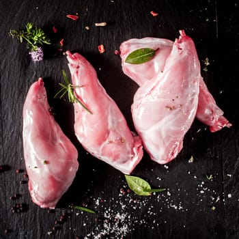Three raw wild rabbit haunches seasoned with herbs and spices ready for grilling, overhead view with copyspace