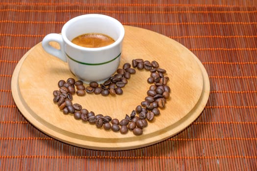 A cup of coffee on wood with seeds around drawing an heart