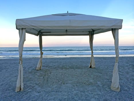 A cabana with it's sides tide back on the beach at sunset