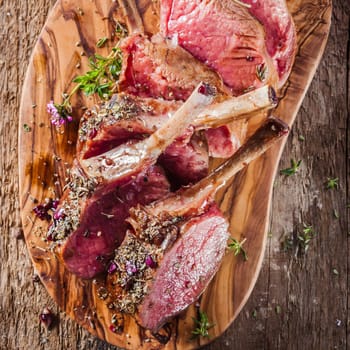 High Angle View of Rare Rectangle Lamb Chops Sliced and Seasoned with Fresh Herbs on Wooden Cutting Board