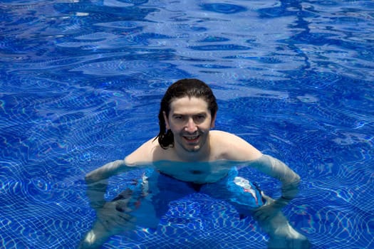 Young happy man smiling on a pool with clear blue water