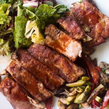Top view close-up food photo of barbecue pork ribs with vegetable garnish.