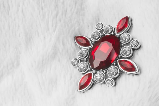 Beautiful luxurious brooch jewel or jewelry with ruby red gemstone on white fur background.
