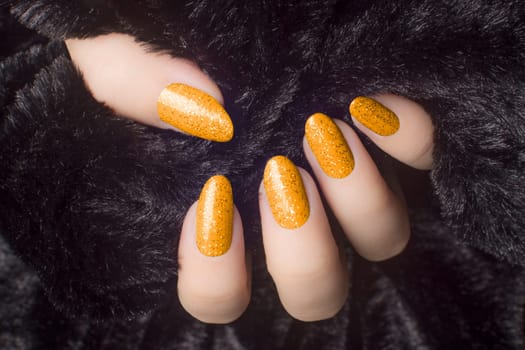 Female hand with glittered orange nails is holding black fur, manicure and nail care concept.