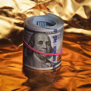 A roll of one hundred American dollars in close-up on a gold background. A big pile of cash dollars. One hundred dollar bills. Close-up, free space for captions and text.