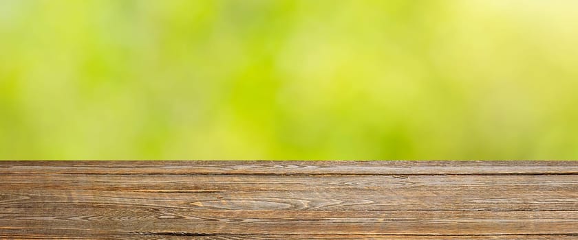Background with blurred green leaves and empty wooden planks in the foreground. For product demonstrations, free space, layout, mockup, perspective board, background board.