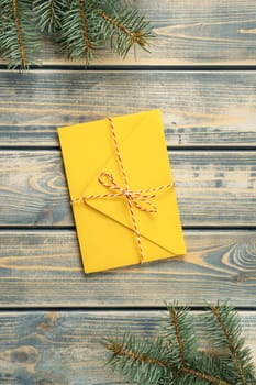 Yellow envelope on gray wooden background with branches of Christmas tree. New year envelope tied with cord with bow. Top view. Vertical