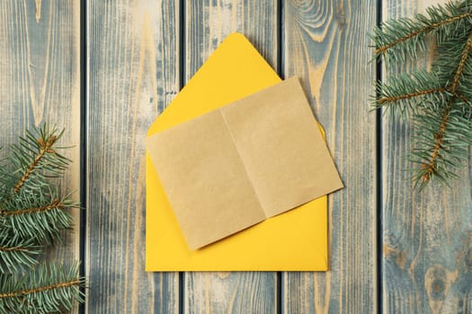 Yellow bright open envelope on gray wooden background with blank kraft paper greeting card with branches of Christmas tree. New year envelope. Copy space. Top view