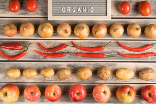 Food composition of onion bulbs, chilly pepper, apples, tomatoes, potato on shelves with nameplate organic. Organic food and fresh vitamin meal in market, store. Top view, mockup, flat lay, full frame