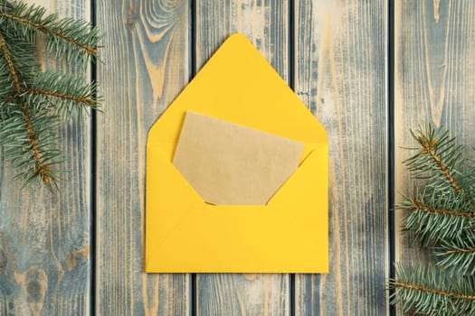 Yellow bright open envelope on gray wooden background with blank kraft paper greeting card with branches of Christmas tree. New year envelope. Copy space. Top view