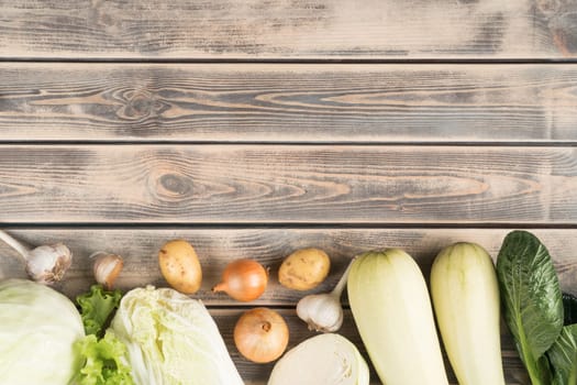 Vegan food composition of onion, cabbage, zucchini, squash marrow, garlic vegetables on wooden background. Grocery store. Vegetarian farm produce. Balanced food flyer, Copy space, top view, flat lay