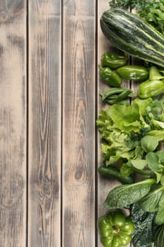 Vertical green food composition of organic, natural garden vegetables on wooden background. Zucchini, cucumber and pepper with parsley. Farm production. Health care produce. Copy space, top view