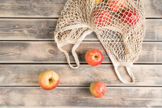 Scattered fresh red raw apples from string bag on wooden table background. Rustic, rural and ecological produce. Antioxidant, detox and vitamin food. Ecological care. Top view, flat lay, copy space