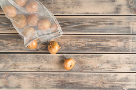 Composition of raw fresh onion bulbs in transparent packet or bag on wooden background. Bio organic food, rustic meal. No additives, health care and market distribution. Top view, layout, copy space