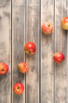 Vertical photo of scattered fresh red raw apples on wooden table background. Rustic, rural and ecological produce. Antioxidant, detox and vitamin food dieting. Top view, flat lay, copy space