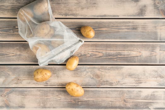 Composition of raw fresh potato in transparent packet on wooden background. Degradable package, zero waste and ecological, sustainable lifestyle. Zip pack, bio organic material. Top view, copy space