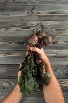 Vertical unrecognizable cropped man hands holding raw fresh clean beetroots with stems and leaves on wooden background. Healthy nutrition, diet for good digestion. New recipe. Top view, copy space