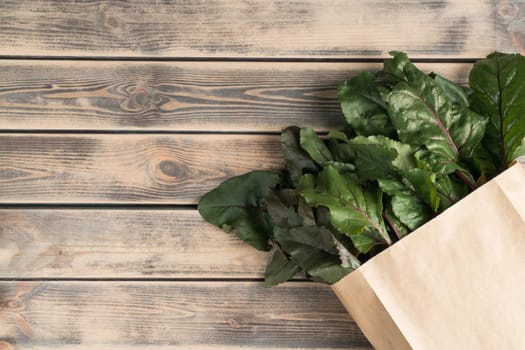 Lush green foliage and stems of beet roots hiding in eco bag, package on wooden background. Ecological shopping, food delivery and organic farm vegetable market, store. Top view, copy space