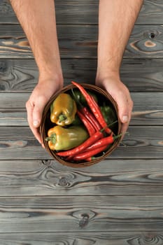 Vertical close up photo of unrecognizable cropped man hands holding fresh, juicy green bell pepper vegetable on wood table background. Rustic freshness, agriculture season. Top view, above, copy space