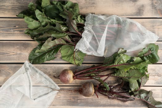 Composition of raw fresh clean beetroots with stems in special organic degradable transparent bags on wooden background. Healthy nutrition, detox diet for good immune system. Top view, copy space