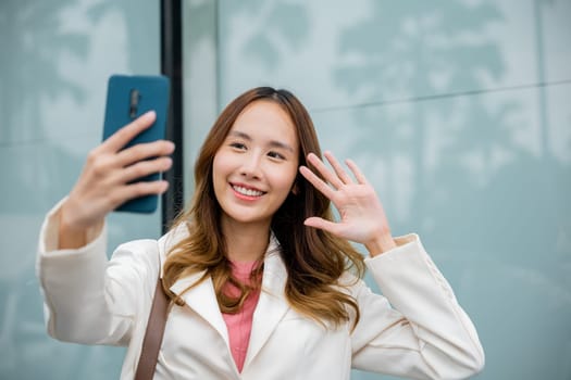 Lifestyle and technology. Young Asian businesswoman during talking video chat in smart mobile phone outside in the city next the building, Happy business woman enjoying sunlight outdoors. Say hello