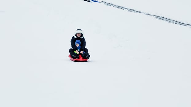 Mom and baby enjoy a sleigh ride. Sledding for children. Child riding a sleigh. Children play outdoors in the snow. Outdoor fun for family Christmas holidays.