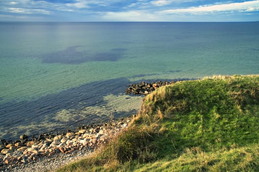Hundested, Denmark on the cliff overlooking the sea. Baltic Sea coast, grassy meadow, beach. Clouds on horizon. Landscape photo from Scandinavia.