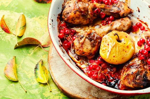 Barbecued chicken drumsticks in a baking dish with apple and berries. Autumn meat recipe.