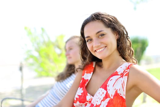 Happy woman with a friend looking at camera sitting in a bench