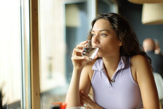 Distracted woman drinking water in a restaurant looking away through a window