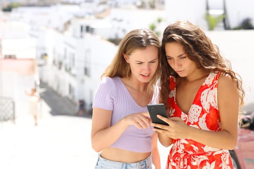 Two worried tourists checking smart phone online news on summer vacation