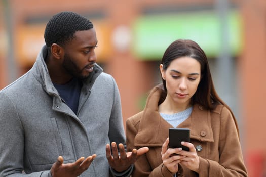 Woman using smart phone ignoring her friend in the street in winter