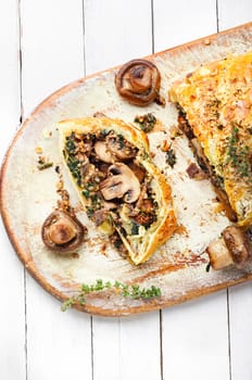 Closed homemade mushroom pie. Sliced savoury mushroom champignons pie on old kitchen board