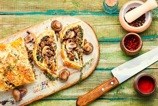 Closed homemade mushroom pie. Sliced savoury mushroom champignons pie on old kitchen board