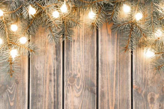 Burning lit light bulbs of Christmas tree branches garland lying on old plank surface. Rustic holiday background, copy space. Merry Christmas and Happy New Year