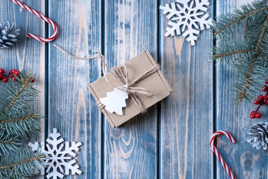 Kraft cardboard gift box tied with rough jute rope on gray wooden background with branches of Christmas tree and Christmas decorations. Top view
