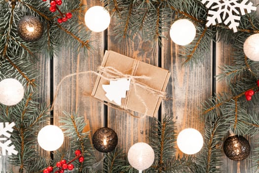 Kraft xmas cardboard gift box tied with jute rope in Christmas tree branch garland frame with flickering light bulbs of thread balls. Happy new year, merry christmas. Top view