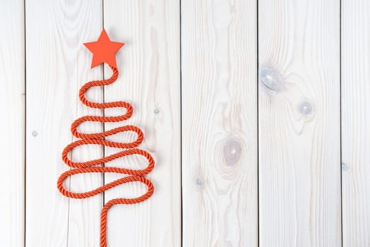 Red twisted cord folded in shape of Christmas tree with star on top. Fir tree on white wooden surface. Top view, copy space, place for text. Merry Christmas, Happy New Year greeting card