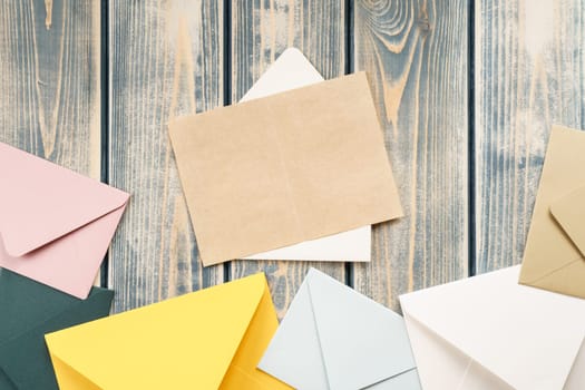 White open envelope with open kraft paper card on gray wooden background. Multicolored envelopes lie side by side. Copy space. Top view. Mail, correspondence, sending messages, congratulations
